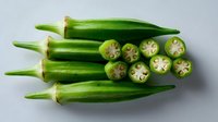 Fresh green okra pods arranged on light background, whole and cross-sectioned showing distinctive star pattern inside, natural organic produce for cooking.