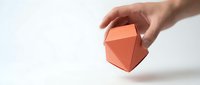 Hand holding orange geometric polyhedron shape against clean white background for modern design projects and creative presentations.