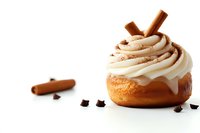 Fresh cinnamon roll with creamy vanilla frosting swirls, topped with cinnamon stick and chocolate pieces on white background, isolated pastry photography.