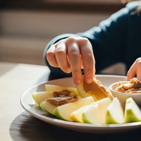 Person dipping fresh apple slices in caramel sauce at wooden table. Healthy snack with sweet treat for afternoon break or dessert time.