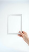 Female hand holding blank white picture frame against neutral wall background for mockup and presentation purposes.