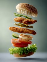 Levitating layers of crispy chicken burger with fresh vegetables and sesame bun captured in dynamic composition against moody background. Creative food photography.