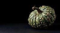 Green striped decorative gourd with textured ridged surface isolated on dark background, suitable for autumn harvest designs and seasonal marketing materials.