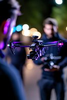 Professional camera drone with purple LED lights hovers during night filming session, bokeh lights in background create atmospheric cinematic mood.
