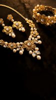 Elegant gold jewelry set with floral motifs, pearls and crystals including necklace, bracelet and earrings on dark background for luxury fashion.