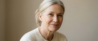 Senior woman with white hair wearing cream sweater, smiling warmly at camera against neutral beige background. Portrait suitable for healthcare, wellness, lifestyle and aging gracefully concepts.