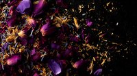 Dried purple rose petals and golden flower fragments scattered on dark background, creating dramatic contrast and moody botanical composition for wellness designs.