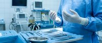 Surgeon in blue scrubs putting on sterile gloves in operating room with surgical instruments on tray, ready for procedure.