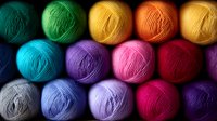 Colorful yarn balls arranged in rows showcasing vibrant rainbow colors from turquoise to purple. Soft wool texture and natural lighting create depth and warmth for craft projects.