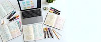 Flat lay of open notebooks with colorful mind maps, markers, and a laptop on a white desk, showcasing creative planning and study workspace.