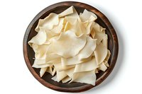 Fresh coconut slices in wooden bowl, raw white pieces of tropical fruit meat arranged on rustic serving dish, top view food photography.