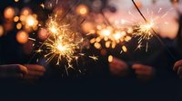 Glowing sparklers burst with golden light against dark background, creating festive celebration atmosphere for holiday events, parties, and New Year festivities.