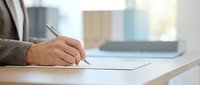 Businessman signing document at desk with laptop in background, professional office workspace for business contracts and agreements.