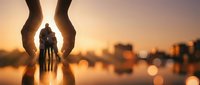 Protective hands surrounding silhouette of family at sunset with warm bokeh city lights reflecting on water creating emotional security concept.