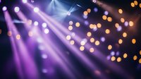 Purple and orange stage lights create dramatic atmosphere with bokeh effect and diagonal light beams cutting through hazy air, setting mood for concert or theater performance.