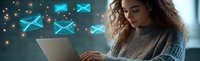 Young Hispanic woman with curly hair using laptop with glowing blue email icons floating above, working from home in cozy sweater during evening hours.