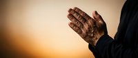 Hands pressed together in prayer position against warm golden sunset background, spiritual meditation and faith concept for religious content.