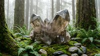Large smoky quartz crystal cluster formation surrounded by moss-covered stones in misty forest setting with tall trees and ferns for meditation and healing.