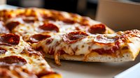 Close-up view of hot pepperoni pizza with melted mozzarella cheese and tomato sauce, showing crispy crust and glistening toppings in warm lighting.