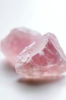 Raw rose quartz crystal formation with translucent pink hues and natural geometric angles captured in soft lighting against white background, showing mineral's raw texture.