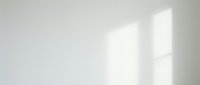 Minimalist interior with soft natural light casting geometric window shadows on neutral white wall, suitable for backgrounds and design projects.