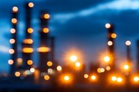 Defocused industrial night scene with glowing orange lights and smokestacks against deep blue twilight sky, creating atmospheric bokeh effect for background designs.
