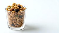 Homemade granola with oats, nuts and dried fruits in glass cup on white background. Healthy breakfast cereal mix for morning meal and snacking.