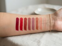 Lipstick color swatches on woman arm showing red pink nude shades for makeup testing and cosmetic product selection in natural light.