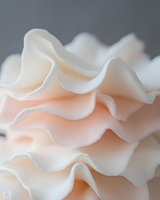Delicate ruffled fabric layers in soft peach and cream tones creating flowing waves with gentle curves and organic textures for elegant design projects.
