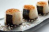 Fresh onigiri rice balls wrapped in nori seaweed, topped with spicy seasoning and sesame seeds, served on black ceramic plate. Japanese cuisine.