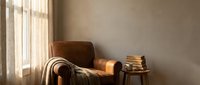 Cozy reading corner with brown leather armchair, soft throw blanket and stack of books by sunny window creating warm atmospheric home interior for relaxation.