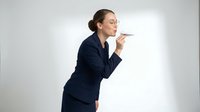 Young professional woman with dark hair in business attire blowing a paper airplane, symbolizing innovation, ideas, and forward-thinking business concepts for corporate communications.