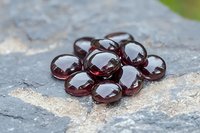 Red glass pebbles arranged in flower shape on gray stone surface, reflecting light with glossy finish. For garden decor and artistic compositions.
