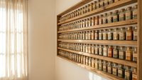 Organized spice rack with glass jars containing various herbs and seasonings mounted on wooden shelves in modern kitchen interior for culinary storage solutions.