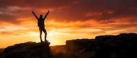 Silhouette of person with raised arms celebrating success on mountain peak during dramatic orange sunset sky. Achievement and triumph concept for motivation.