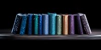 Row of colorful metallic books with glitter sparkles arranged in curved line against dark background, creating dramatic lighting effect and reflective surface.