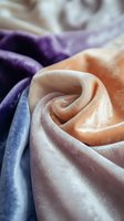 Luxurious silk fabric in peach, purple and blue colors creating soft folds and waves with elegant sheen and texture, suitable for fashion and textile backgrounds.