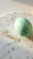 Mint green painted Easter egg with gold speckles on a marble plate with elegant gold script lettering, soft natural light.