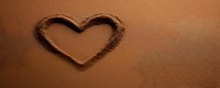 Heart shape drawn in smooth sand surface with soft lighting creating romantic beach atmosphere for love and relationship concepts.