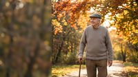 Senior Caucasian man with walking cane strolling through autumn park with golden foliage, enjoying peaceful outdoor exercise and healthy aging lifestyle.