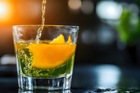 Whiskey pouring into glass with orange slice garnish, golden liquid splashing against citrus in dark bar setting.