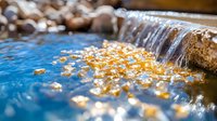 Autumn leaves floating on blue water surface near small waterfall cascade, creating natural tranquil scene with gentle water movement and seasonal atmosphere.