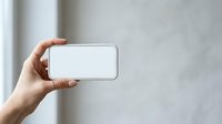 Person with medium skin tone holding smartphone horizontally with blank white screen for app mockups, web design presentations, or mobile technology advertising campaigns.