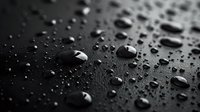 Water droplets scattered on dark hydrophobic surface create dramatic macro photography composition with light reflection and condensation pattern.