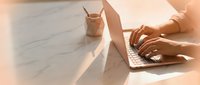 Woman hands typing on laptop computer at modern workspace with coffee cup in warm sunlight for remote work and productivity concepts.