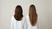 Two women with different hair lengths standing back to camera wearing white shirts against neutral background for hair care comparison concept.