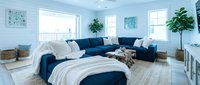 Modern bedroom with navy blue sectional sofa, white bedding, potted plants, and bright windows creating a serene coastal-inspired living space for home decor design projects.