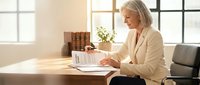 Senior Caucasian businesswoman reviewing financial documents at modern office desk with natural lighting for corporate and professional content.