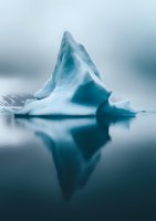 Majestic blue iceberg floating in calm arctic waters with mirror reflection against misty background, showcasing nature's raw power and tranquility.