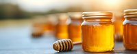 Fresh raw honey in glass jars with wooden dipper on rustic table against blurred natural background. Golden organic sweetener for healthy eating.